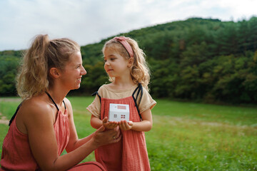 Wall Mural - Little girl with her dad holding paper model of house with solar panels.Alternative energy, saving resources and sustainable lifestyle concept.