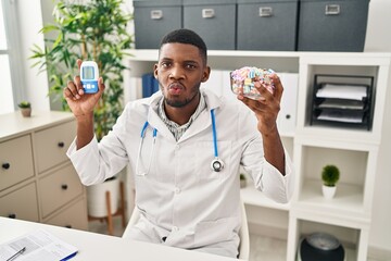 Wall Mural - African american doctor man using glucose meter looking at the camera blowing a kiss being lovely and sexy. love expression.