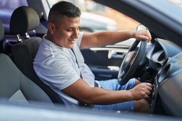 Wall Mural - Young latin man sitting on car turning on radio at street