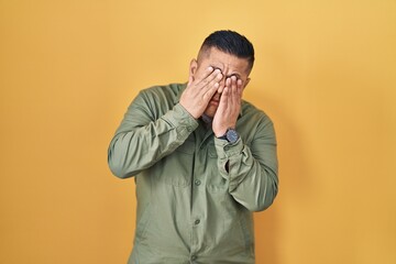 Sticker - Hispanic young man standing over yellow background rubbing eyes for fatigue and headache, sleepy and tired expression. vision problem