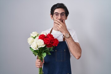 Poster - Young hispanic man holding bouquet of white and red roses laughing and embarrassed giggle covering mouth with hands, gossip and scandal concept