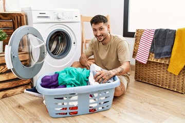 Wall Mural - Young hispanic man smilig confident using washing machine at laundry room