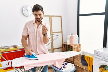 Poster - Young man with beard ironing clothes at home doing money gesture with hands, asking for salary payment, millionaire business