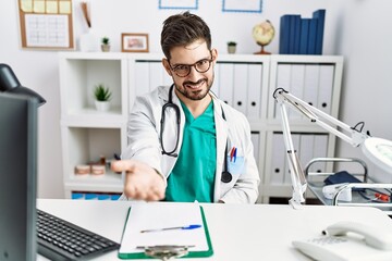 Poster - Young man with beard wearing doctor uniform and stethoscope at the clinic smiling cheerful offering palm hand giving assistance and acceptance.