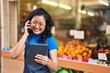 Young chinese woman employee talking on the smartphone using touchpad at fruit store
