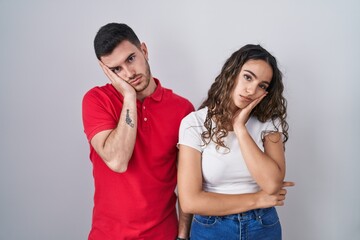 Wall Mural - Young hispanic couple standing over isolated background thinking looking tired and bored with depression problems with crossed arms.