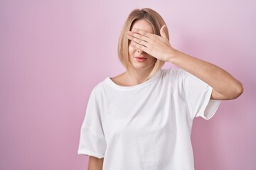 Sticker - Young caucasian woman standing over pink background covering eyes with hand, looking serious and sad. sightless, hiding and rejection concept