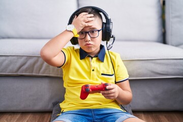 Sticker - Young hispanic kid playing video game holding controller wearing headphones worried and stressed about a problem with hand on forehead, nervous and anxious for crisis