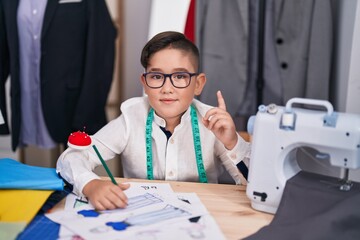 Sticker - Young hispanic kid at tailor room surprised with an idea or question pointing finger with happy face, number one