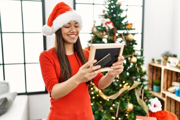 Sticker - Young latin woman looking photo standing by christmas tree at home