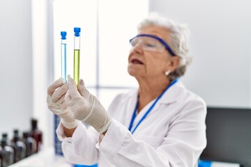 Wall Mural - Senior grey-haired woman wearing scientist uniform holding test tubes at laboratory