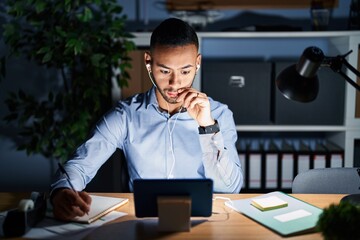 Wall Mural - Young hispanic man working at the office at night mouth and lips shut as zip with fingers. secret and silent, taboo talking