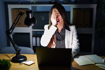 Canvas Print - Young brunette woman working at the office at night with laptop yawning tired covering half face, eye and mouth with hand. face hurts in pain.