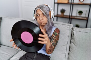 Poster - Middle age grey-haired woman listening to music holding vinyl disc at home puffing cheeks with funny face. mouth inflated with air, catching air.