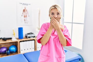 Wall Mural - Young caucasian woman working at pain recovery clinic shocked covering mouth with hands for mistake. secret concept.