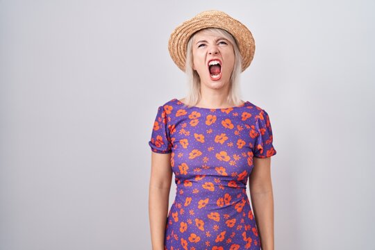 young caucasian woman wearing flowers dress and summer hat angry and mad screaming frustrated and fu