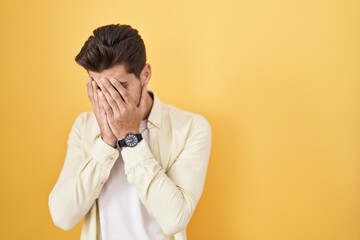 Wall Mural - Young hispanic man standing over yellow background with sad expression covering face with hands while crying. depression concept.