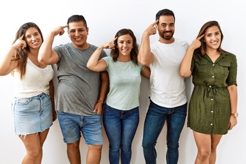 Sticker - Group of young hispanic friends standing together over isolated background smiling pointing to head with one finger, great idea or thought, good memory