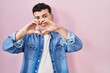 © Krakenimages.com - Non binary person standing over pink background smiling in love showing heart symbol and shape with hands. romantic concept.