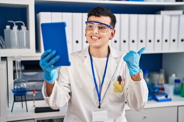 Wall Mural - Non binary person working at scientist laboratory using tablet pointing thumb up to the side smiling happy with open mouth