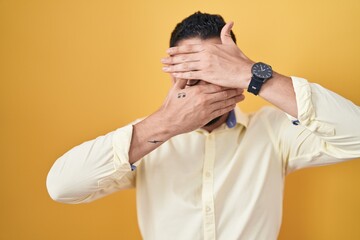 Poster - Hispanic young man wearing business clothes and glasses covering eyes and mouth with hands, surprised and shocked. hiding emotion