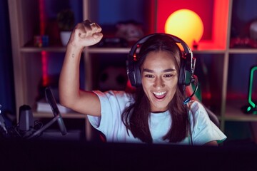 Wall Mural - Young beautiful hispanic woman streamer playing video game with winner expression at gaming room