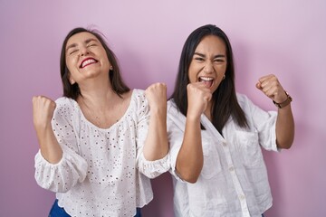 Poster - Hispanic mother and daughter together celebrating surprised and amazed for success with arms raised and eyes closed. winner concept.