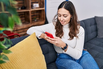 Poster - Young beautiful hispanic woman using smartphone lying on sofa at home