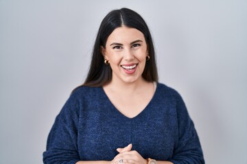 Poster - Young brunette woman standing over isolated background with hands together and crossed fingers smiling relaxed and cheerful. success and optimistic