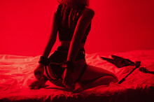 Woman With A Sexy Ass With Handcuffed Hands Sits Erotically On Bed In Bedroom. BDSM Concept Of Sex With Submission And Domination With Erotic Toys