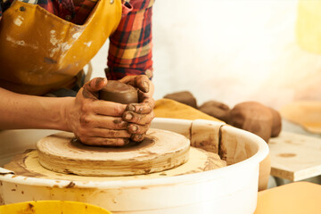 A Potter works with red clay on a Potter's wheel in the workshop..Women's hands create a pot. Girl sculpts in clay pot closeup. Modeling clay close-up. Warm photo atmosphere. 