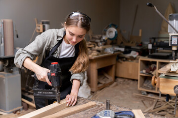 Portrait of a female carpenter using tools for making furniture in a furniture factory. with modern tools