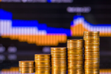 Stacks of golden coins on the background of a blurred business financial graph. Digital business and stock market financial indicator.