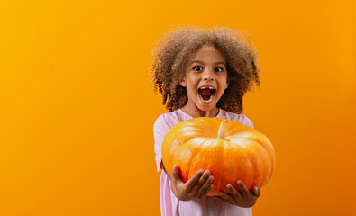 A laughing black girl holds a pumpkin on a yellow background before the Halloween holiday.