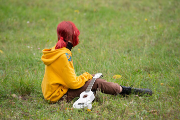 Child in the park with ukulele in white color. Autumn park with yellow foliage.