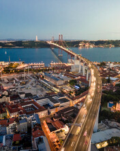 Aerial View Of April 25th Bridge With Christ The King Statue (Cristo Rei) In Background At Sunset, View Of Lisbon Skyline At Night, Alcântara, Lisbon, Portugal.