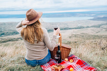 Young Woman With Glass Of Wine Having Picnic In Mountains On Autumn Day, Back View