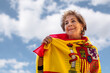 © Fran Rodríguez - Older lady smiling, surrounded by the flag of Spain on a blue background with clouds. Pride of being Spanish. Love and patriotism. Columbus day