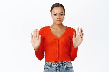 Serious young black woman showing stop gesture, raising palms hands up, prohibit something, rejecting, standing over white background