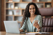 © Prostock-studio - Happy middle eastern woman sitting at workdesk, using smartphone