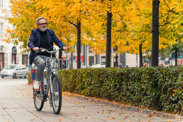 Full-length outdoor shot. Business-casual looking caucasian man in eyeglasses happily cycling through his favorite city park where trees are changing the color of their leaves. High quality photo