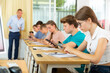 © JackF - Concentrated teenage girl with group of fellow students sitting at lesson in classroom, using mobile phone