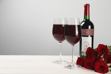 Poster - Bottle and glasses of red wine near beautiful roses on white wooden table. Space for text