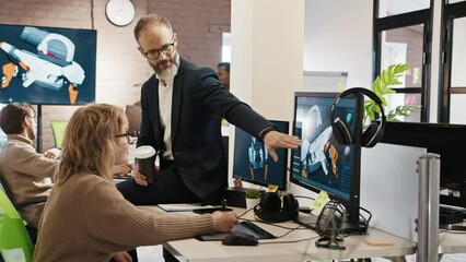 The CEO of the company studio developers of games and applications discusses with the artist a 3D model on a computer against the background of other employees of the company.