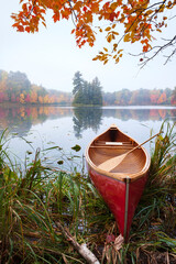 Wall Mural - red wooden canoe on calm lake with trees in fall color and maple branches above during autumn