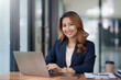 © amnaj - Happy young asian businesswoman sitting on her workplace in the office. Young asian woman working at laptop in the office.