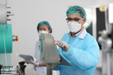 Poster - Inspector woman and colleague man working on quality of mask and medical face mask production line, Industry and factory concept.