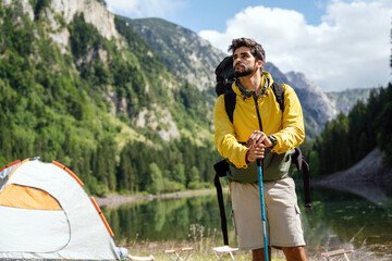 Hiker young man with backpack and trekking poles looking at the mountains in outdoor