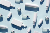 Pattern made with white bottles and jars of cosmetic products and strong shadow on blue background, as backdrop or texture. Creative layout for your design