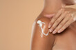 © vladimirfloyd - Close up young woman smearing shoulder with cream over beige background
